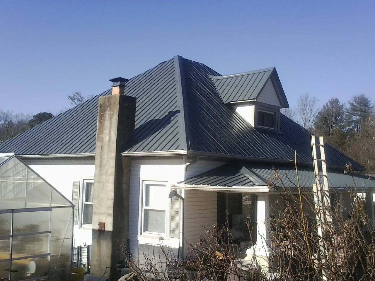 Dark blue standing seam metal roof on a white farmhouse with dormer — Slate & Tile Roof Repair by Roofing Brothers in Kerrville