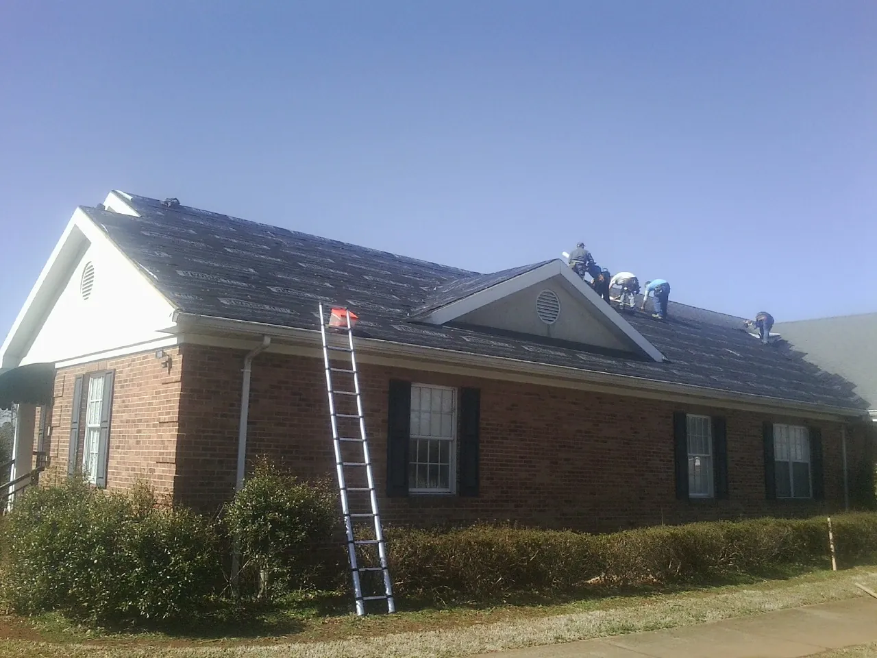 Crew tearing shingles off a brick ranch roof with a ladder set — Metal Roof Repair work by our crew in Kerrville