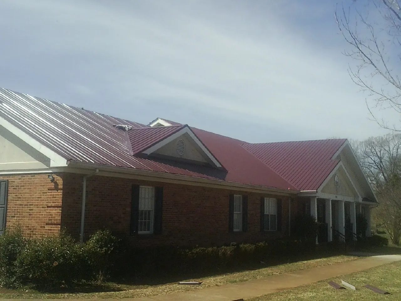 Red metal roof with gabled entries on a long brick building, from a Hail Damage Roof Repair job in Kerrville