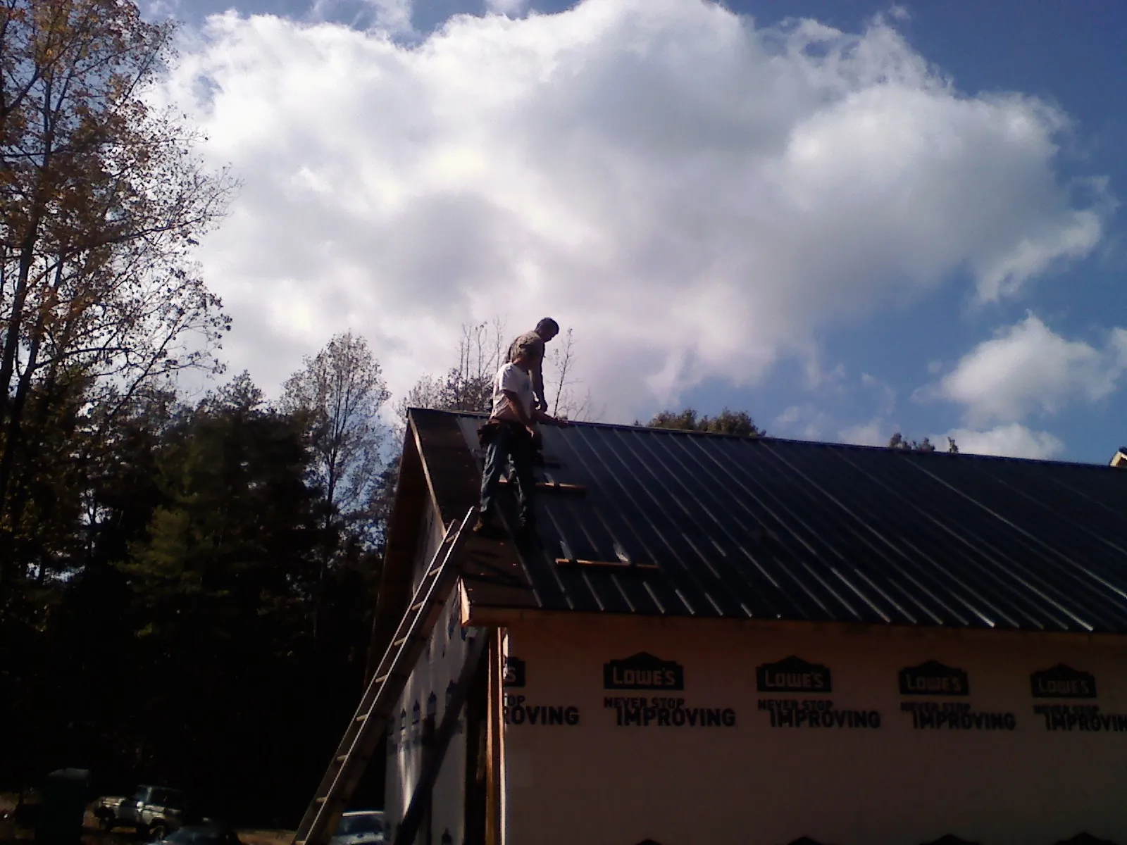 Roofer fastening dark metal panels high against a cloudy sky, from a Roof Inspection job in Kerrville