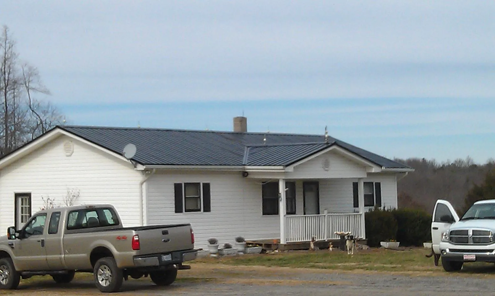 Finished dark metal roof on a white ranch home with work trucks parked in Kerrville