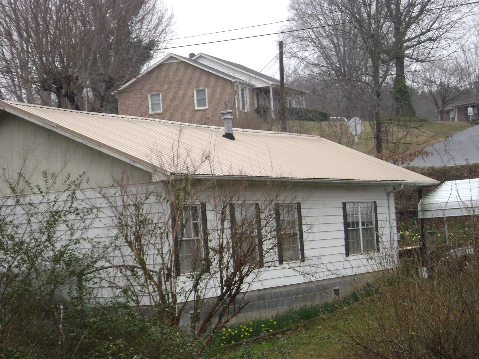 Tan metal roof on a white sided house set into a hillside — Commercial Roofing by Roofing Brothers in Kerrville